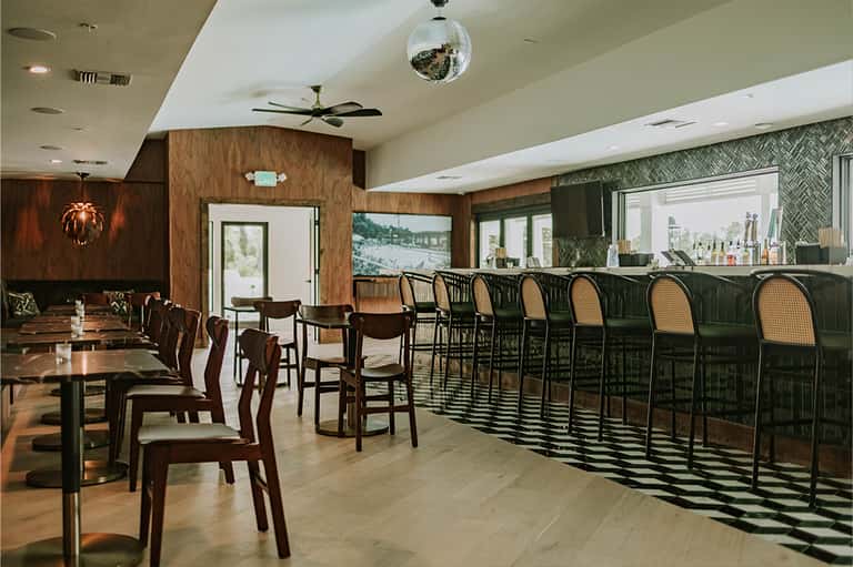 Upscale restaurant and bar interior with wood paneling, dark chairs, and geometric floor patterns