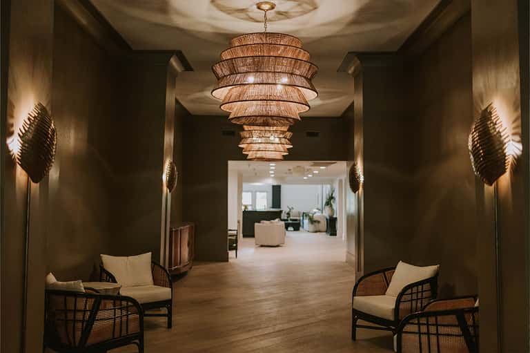Elegant hotel corridor with rattan pendant light, dark walls, and contemporary seating areas