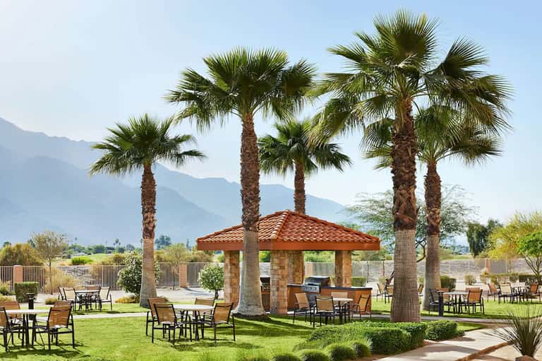 Resort courtyard with palm trees, grass, patio furniture, covered gazebo with red roof, and mountain views