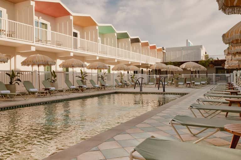 Beachfront resort pool with thatched umbrellas, colorful beach cabins, and loungers