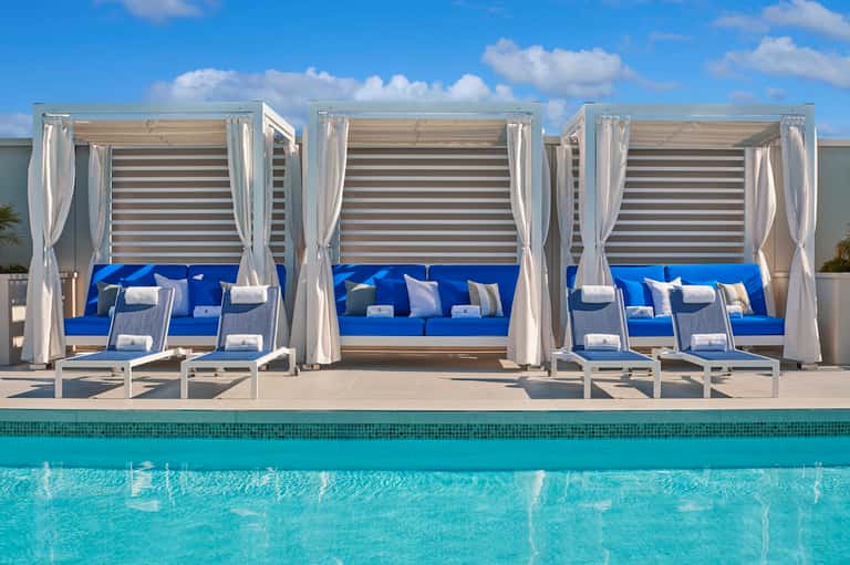 Luxury poolside cabanas with blue cushions and white curtains overlooking turquoise water