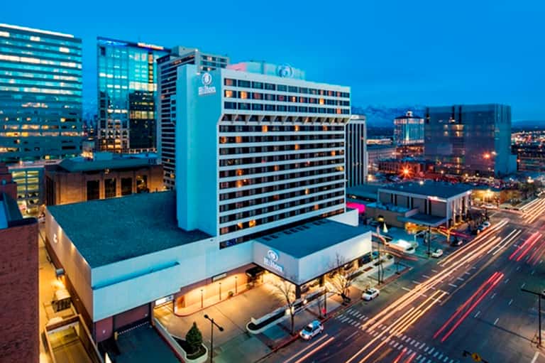 Hilton hotel exterior at dusk with illuminated blue facade and city skyline in background