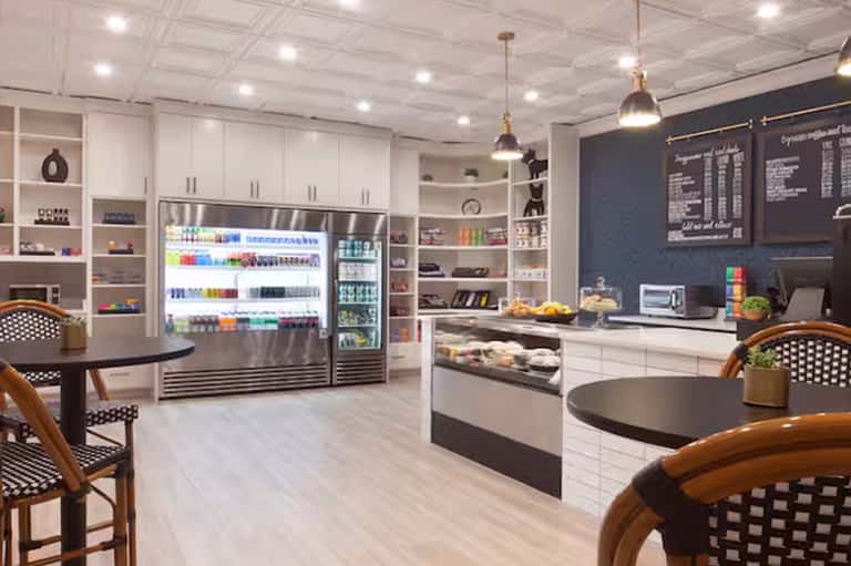 Modern café interior with white cabinetry, refrigerated display cases, black menu boards, and wooden bistro seating
