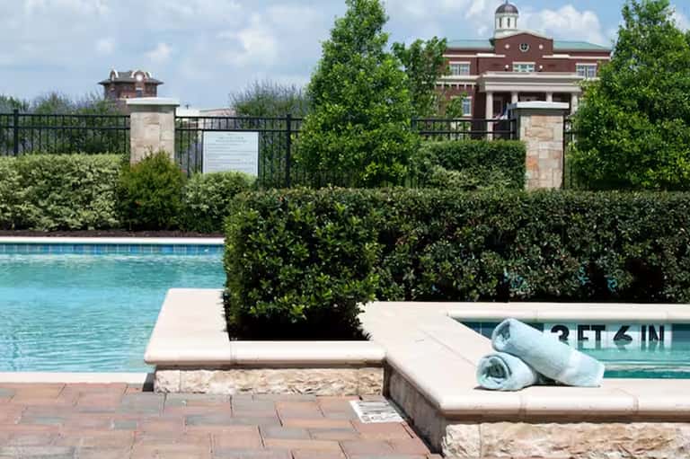 Resort pool with hedge landscaping, towel service, and historic brick building in background
