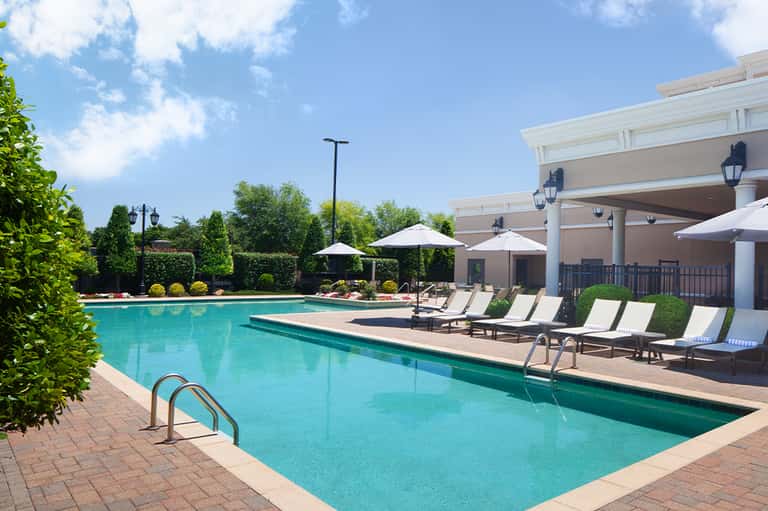 Resort swimming pool with lounge chairs, umbrellas, and modern building