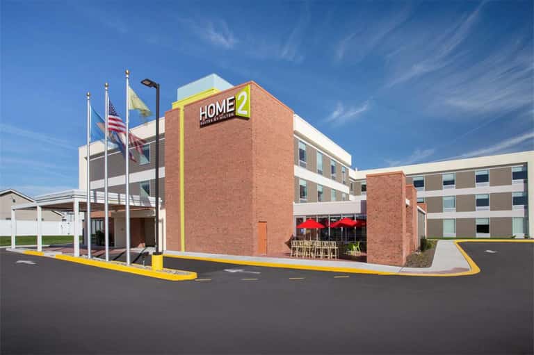 Home2 Suites hotel exterior with brick facade, entrance, and yellow trim under clear blue sky