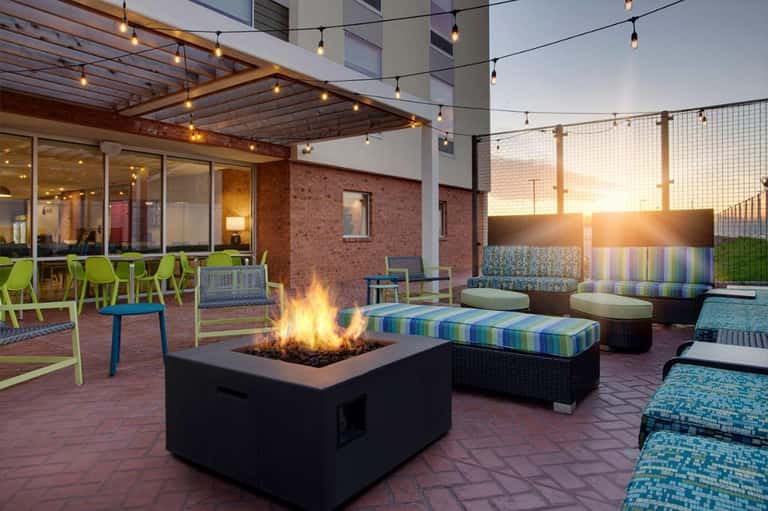 Rooftop terrace with fire pit, colorful striped seating, and brick building at golden hour
