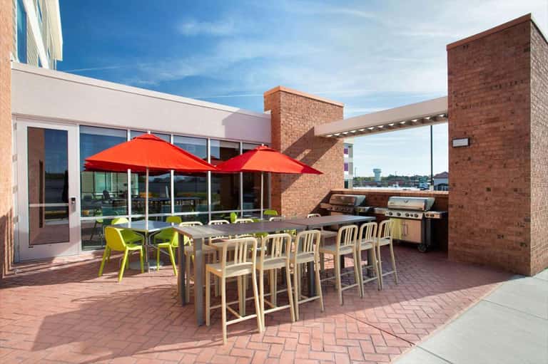 Rooftop terrace with high-top dining table, red umbrellas, and built-in grill area overlooking city skyline