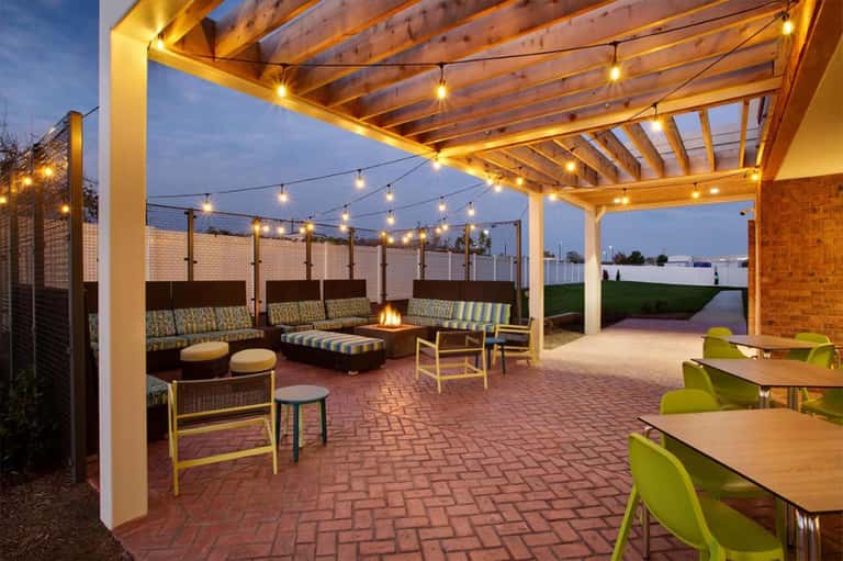Outdoor patio at dusk with pergola, string lights, fire pit, striped seating, and brick flooring