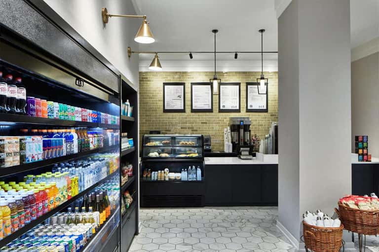 Bright café interior with yellow brick wall, refrigerated display case, beverage coolers, pendant lighting, and wooden baskets