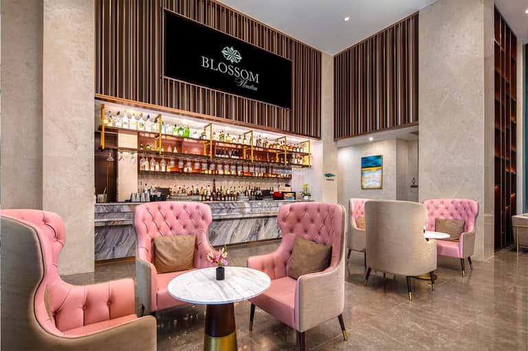 Modern bar lounge with pink tufted chairs, marble tables, and illuminated liquor shelves