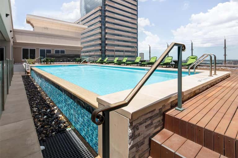 Rooftop pool with blue water, lounge chairs, and city skyline view from elevated deck