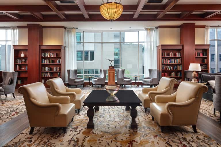 Elegant library lounge with leather chairs, wood bookshelves, coffered ceiling, and city views