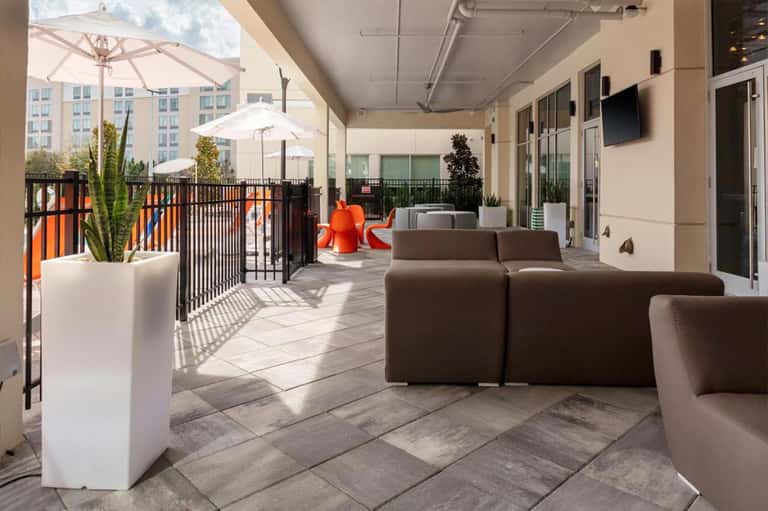 Contemporary rooftop lounge with brown modular seating, white umbrellas, potted plants, and city skyline views
