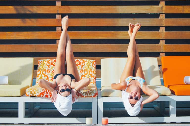 Two people lying on wooden lounge chairs with legs up, wearing white clothing and sunglasses