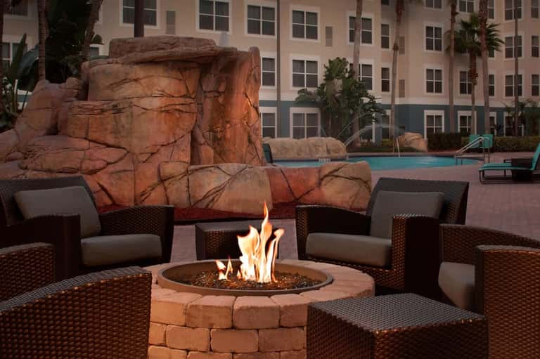 Outdoor fire pit seating area with woven chairs and stone backdrop next to a resort pool