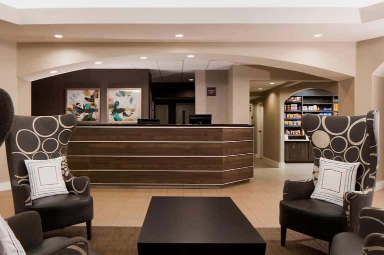 Modern hotel lobby with curved dark wood reception desk, decorative chairs, and contemporary artwork