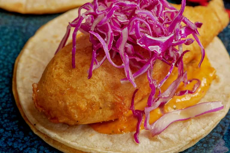 Gourmet taco on white plate topped with crispy fish and purple pickled onions