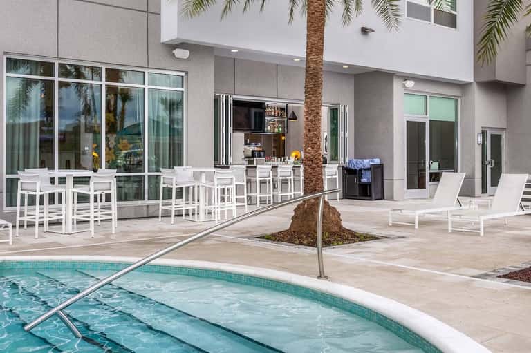 Modern poolside terrace with white bar seating, palm tree, and contemporary building architecture