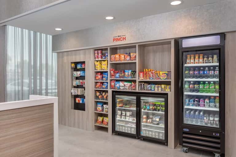 Hotel snack shop interior with wooden cabinetry, refrigerated beverage case, and shelves stocked with packaged snacks