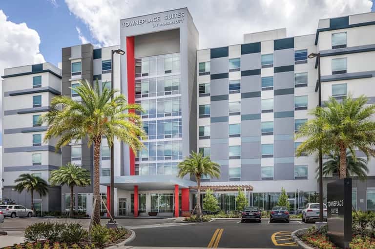 TownePlace Suites hotel exterior with modern white and blue checkered facade, red accents, and palm trees