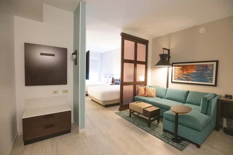 Hotel suite with mint green sofa, separate bedroom, and modern coastal décor