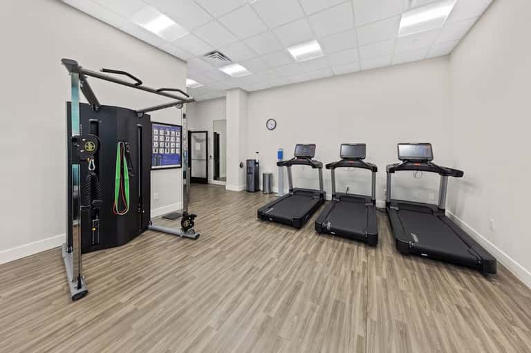 Fitness center with treadmills, exercise equipment, and a cable machine on wooden flooring