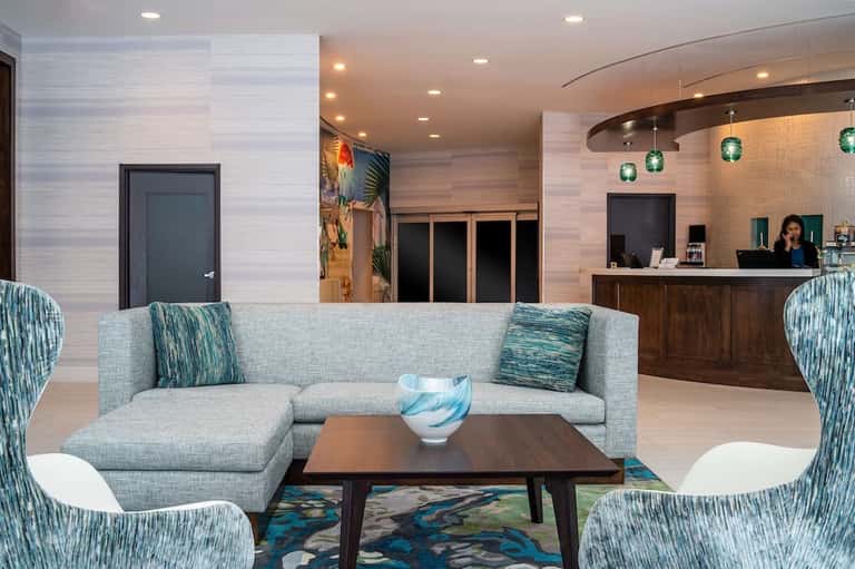 Modern hotel lobby with gray sectional sofa, teal accents, and curved reception desk