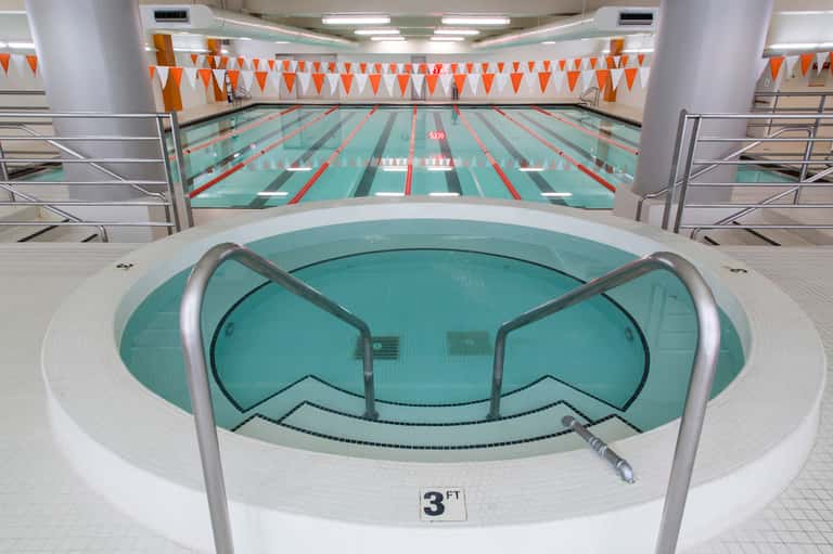 Indoor aquatic center with hot tub in foreground, lap pool behind with lane dividers and orange bunting