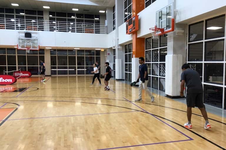 Indoor basketball court with wooden floor, multiple hoops, and people playing