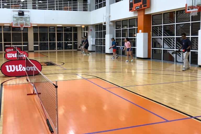 Indoor gymnasium with orange and wood-colored court, basketball hoops, and Wilson branding visible