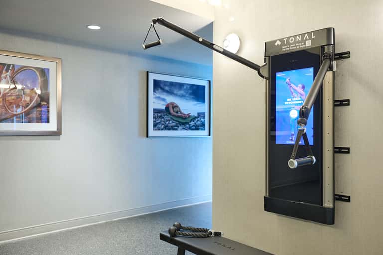 Modern fitness room with blue accent wall, framed artwork, and interactive exercise machine with screen display