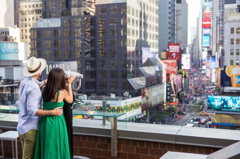 Couple viewing cityscape from observation deck with telescope overlooking Times Square