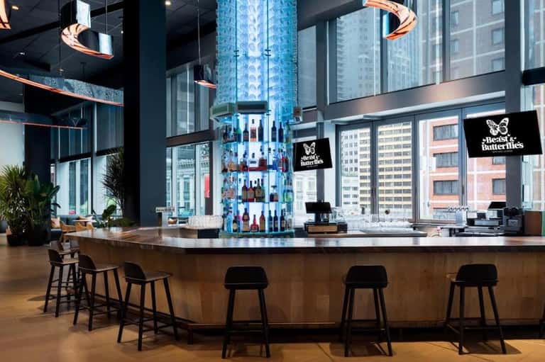 Modern hotel bar with tall bottle display, copper lighting fixtures, and city skyline views