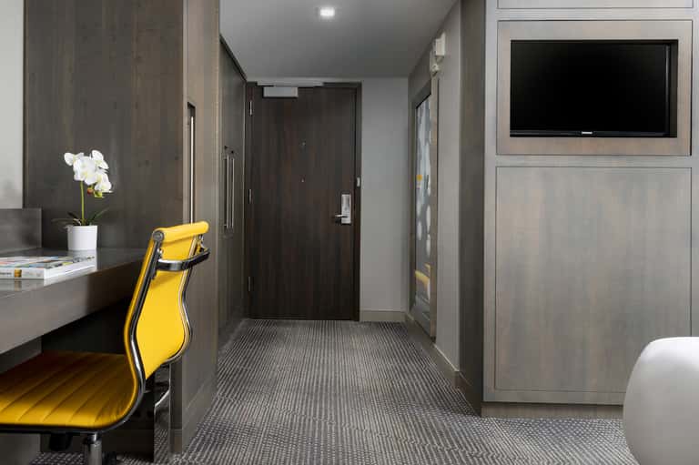 Modern hotel corridor with dark wood paneling, yellow accent chair, and minimalist décor