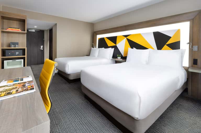 Hotel room with two queen beds, yellow accent headboard, modern furnishings, and contemporary decor