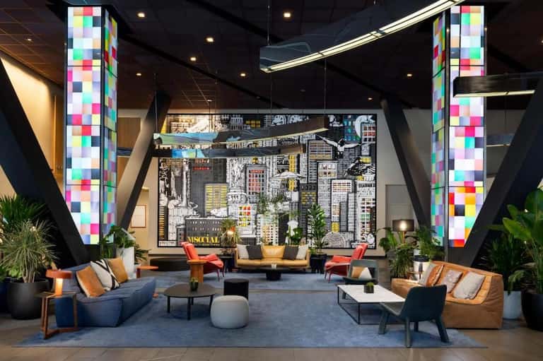 Modern hotel lobby with colorful pixelated columns, city skyline mural, and contemporary furniture arrangement