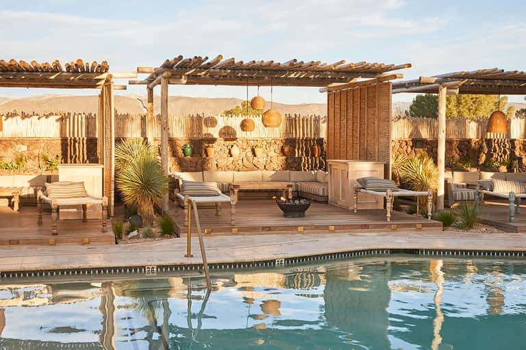 Desert spa pool area with wooden pergola, lounge chairs, and stone wall backdrop at dusk