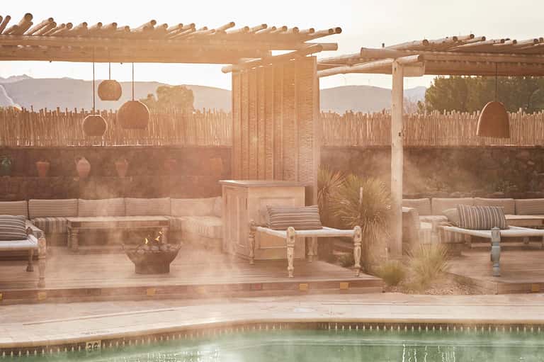 Desert spa lounge with wooden pergola, fire pit, and mineral pool with mountain views