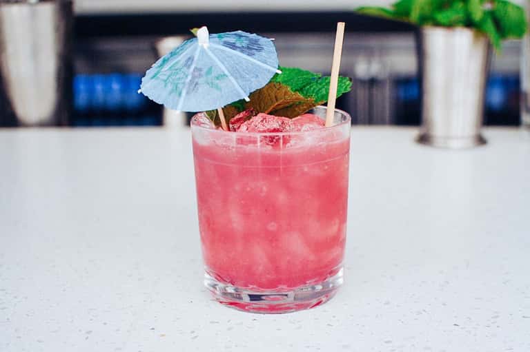 Pink cocktail with blue umbrella and mint garnish on outdoor patio table