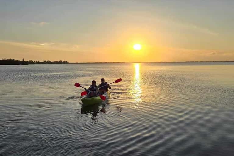 Two people kayaking at golden sunset over calm bay water with distant shoreline