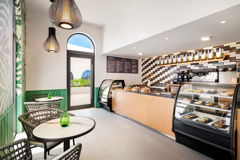 Modern café interior with green accent wall, pendant lighting, counter service, and checkered tile backdrop