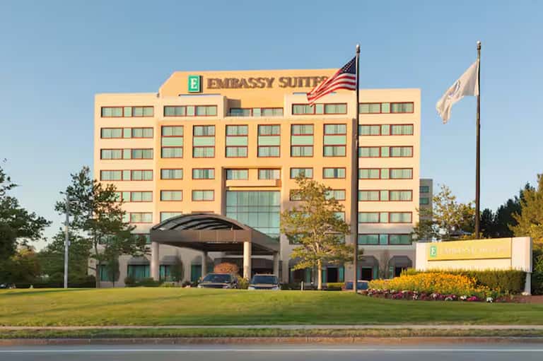 Embassy Suites hotel exterior with yellow facade, American flag, and manicured lawn