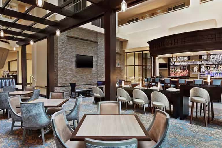 Modern hotel lobby lounge with dark wood beams, stone accent wall, bar, and comfortable seating