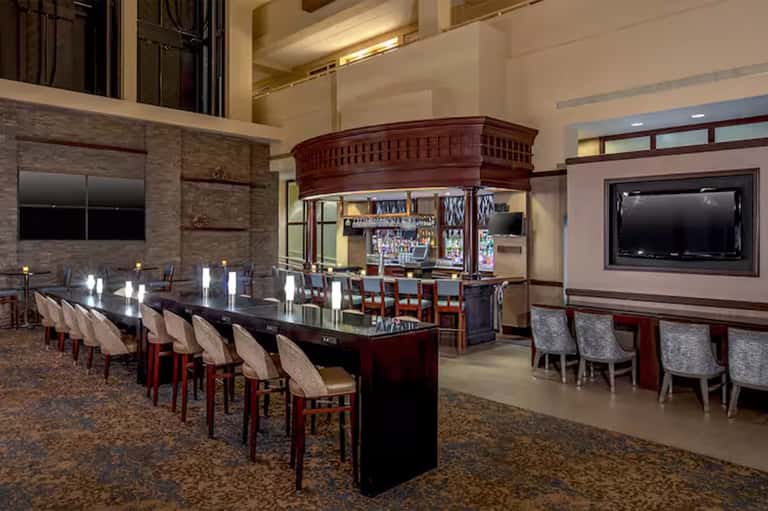 Grand bar lounge with dark wood bar, seating, high ceiling, and ambient lighting