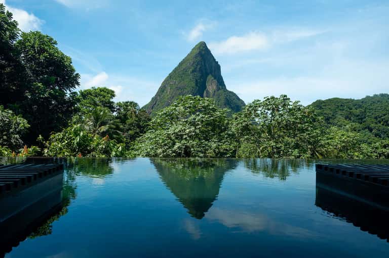 Dramatic mountain peak reflected in still water surrounded by lush tropical forest and wooden docks