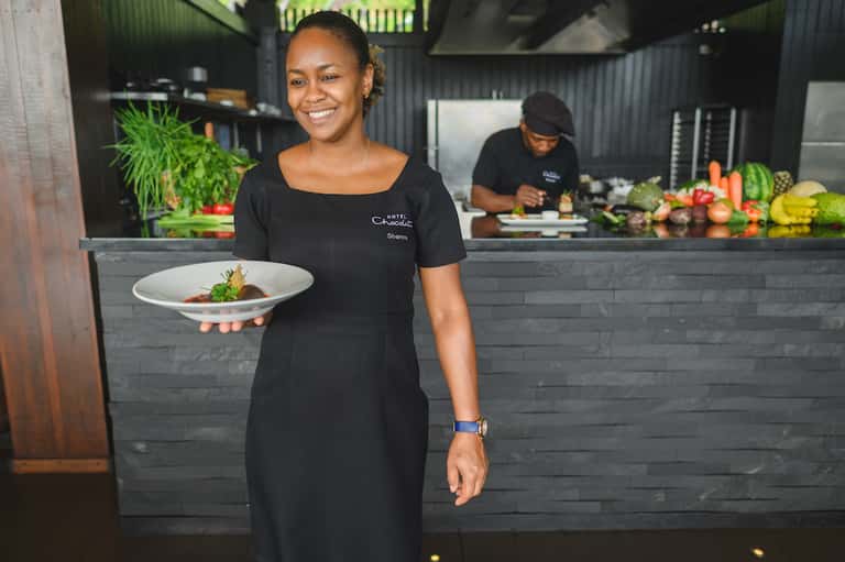 Chef presenting plated dish at modern open kitchen with fresh produce display