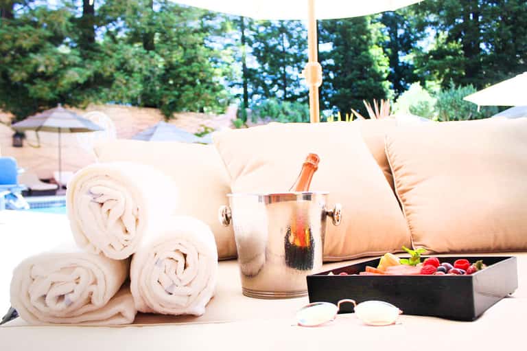 Poolside spa setup with rolled white towels, champagne bottle in ice bucket, and spa essentials on marble table