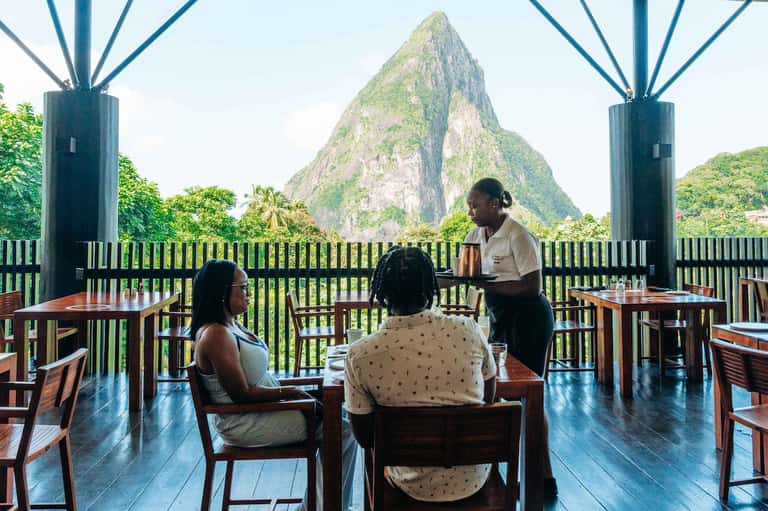 Outdoor dining area with mountain peak view, server attending to guests at wooden tables