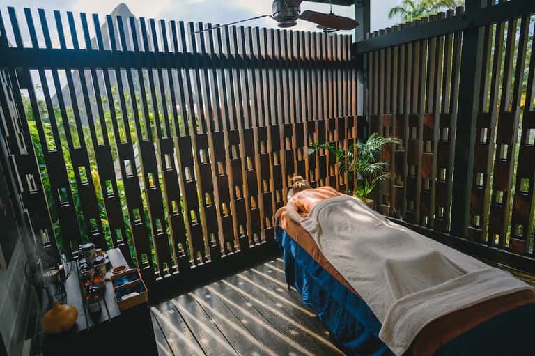 Person relaxing on bed in private balcony with modern slatted railing and tropical greenery